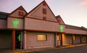 Neon green cactus signs on a stucco building with red trim, at dusk.