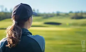 Back view of a woman in a baseball cap on a golf course, looking out at the green.