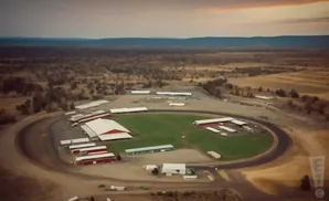 Aerial view of a racetrack with red and white buildings and a green field inside.