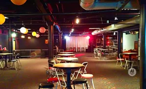 Interior of a dimly lit event space with tables, chairs, and hanging lanterns.