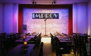 Improv comedy club stage with brick backdrop, microphone, and tables set with candles.