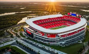 Aerial view of a red and white stadium at sunset with a sunburst effect.