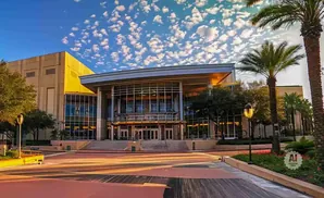 Modern building with large glass entrance, palm trees, and a bright, cloudy sky.