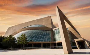 Modern building with a glass facade and angular concrete elements against a sunset sky.