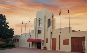 A tan building with large wooden doors and a red awning under a warm, cloudy sunset sky.