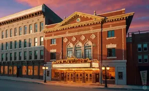 An ornate, vintage theater with a marquee glows warmly under a vibrant sunset sky.