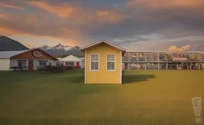 A small yellow building stands in a grassy field with mountains in the background.