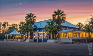 A dark blue building with a metal roof and palm trees at sunset.