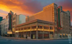 An old theater with marquee signs at sunset, featuring ornate architecture and a warm, colorful sky.