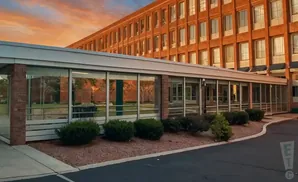 A brick building with a glass walkway in front, set against a sunset sky.
