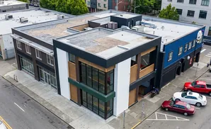 Aerial view of a blue and black building with large windows, parked cars, and a red pickup truck.