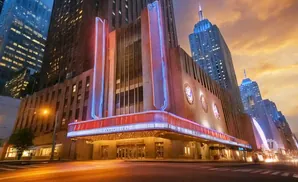 Art deco theater entrance with neon lights framed by skyscrapers at dusk.