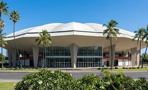 Large, futuristic dome-shaped building with glass facade and palm trees under a bright blue sky.