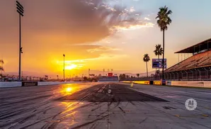 Sunset over a drag strip with stadium seating and palm trees.