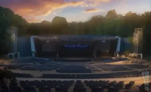 An outdoor amphitheater stage with rows of empty seats under a colorful sunset sky.