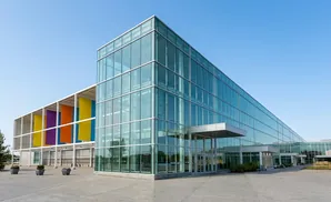 Modern glass building with colorful banners and a clear blue sky.
