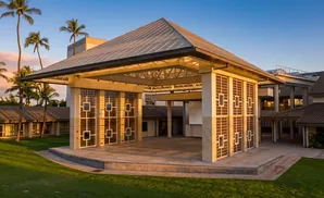 An outdoor stage with a translucent roof and decorative screens, set against a backdrop of palm trees and a sunset sky.