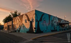 Building corner with a colorful mural of faces and abstract designs at sunset.