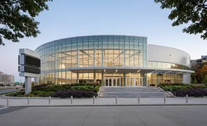 Modern glass-fronted building with tiered steps, landscaping, and a large digital display sign.