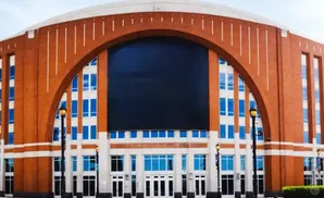 Large brick arena with a massive dark screen above multiple rows of blue windows and white columns.