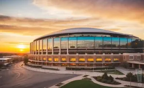 Sunset over a domed stadium with glass walls reflecting the sky.