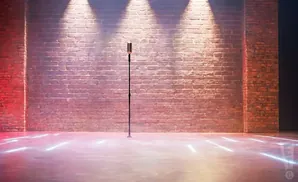 A vintage microphone stands on a stage with a brick wall backdrop and neon floor lights.