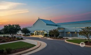 A light blue building with a blue roof at dusk, with a curved road leading to the entrance.