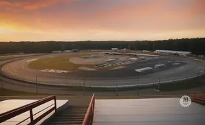 Aerial view of a race track at sunset, with stadium seating in the foreground.