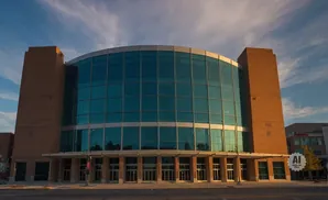 A modern brick and glass building with a curved facade under a blue, cloudy sky.