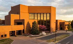 Orange brick building with large windows and trees, at sunset.