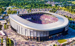 Aerial view of a packed stadium with a curved roof and surrounding parking lots and trees.
