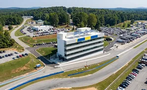 Aerial view of a modern multi-story building at a race track, with parked cars and RVs.
