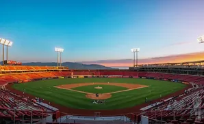 A baseball stadium at sunset with red seats and a green field.