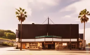 A vintage theater with palm trees and a marquee under a cloudy sky.