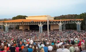 An outdoor amphitheater packed with people enjoying a performance under a covered stage.