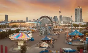 An aerial view of a bustling amusement park with a Ferris wheel, carousel, and other rides, set against a city skyline at sunset.