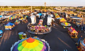 Aerial view of a bustling fairground with rides, tents, food stalls, and crowds of people.