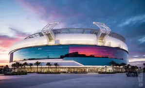 Modern stadium at sunset with colorful sky reflected in glass facade.