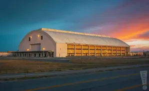 A vast hangar with a curved roof at sunset, the sky awash in blues and oranges.