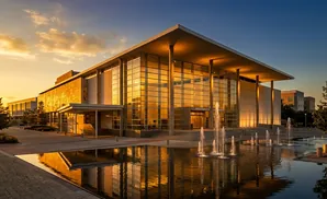 Modern building with glass facade and fountains at sunset.