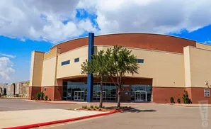 A large building with a curved brick roof and tan and brick walls, with trees and a blue pillar in front.
