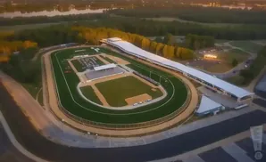 Aerial view of a racetrack with a grandstand, infield, and surrounding trees.