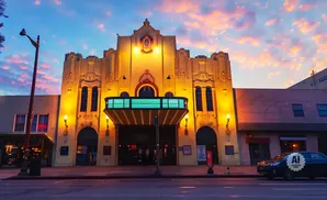 Ornate theater facade with marquee and streetlights illuminated at dusk under a colorful sky.