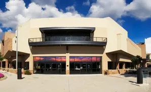 A modern building with a balcony and large glass doors reflecting a sunset sky.