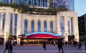 A theater with a red marquee and blue lights is lit up at dusk, with people walking on the sidewalk.