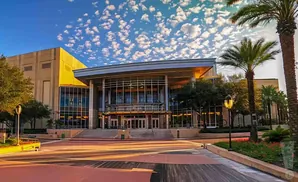 Modern building with large glass entrance and palm trees under a cloudy sky.