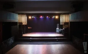 Empty concert hall stage with lighting rig, sound equipment, and a black curtain backdrop.