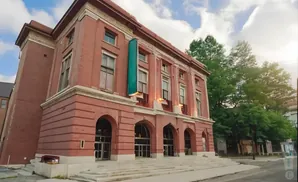 Red brick building with arched entrances and a grand staircase, surrounded by trees.