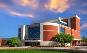 Modern building with brick and glass facade, green lawn, and sunset sky.