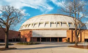 A large, domed building with a brick base, flanked by bare trees under a blue sky with clouds.